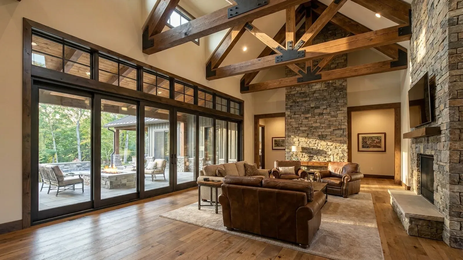 A vaulted barndominium great room with exposed wood trusses, a wall of glazed sliding doors, and a stone-clad fireplace.